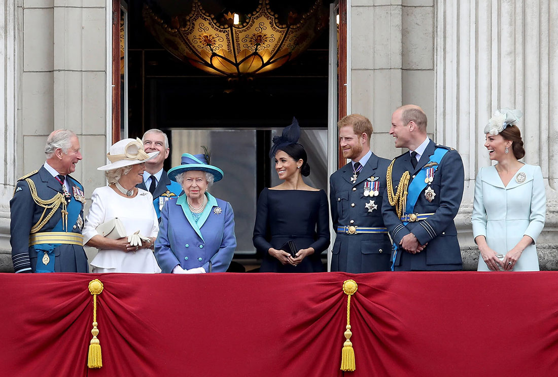 Ratu Elizabeth berdiri di balkon di Istana Buckingham dikelilingi oleh anggota senior keluarga kerajaan termasuk Charles, Camilla, Meghan dan Harry yang semuanya menatapnya sambil tersenyum.  Ratu mengenakan mantel biru dan teal kerajaan dan topi yang serasi dengan bulu hitam.