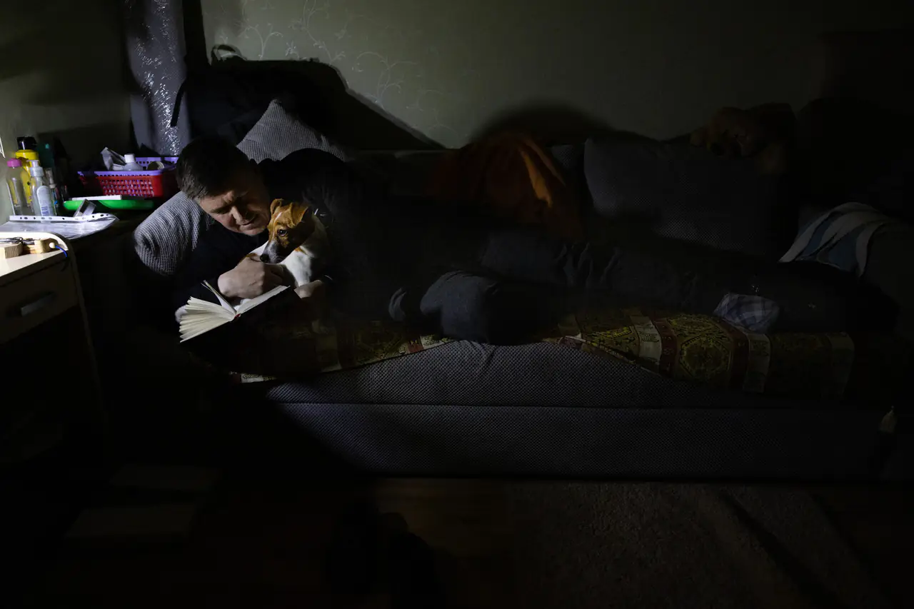 Eduard Yevtushenko reads a book on the couch with his dog during a scheduled power outage.