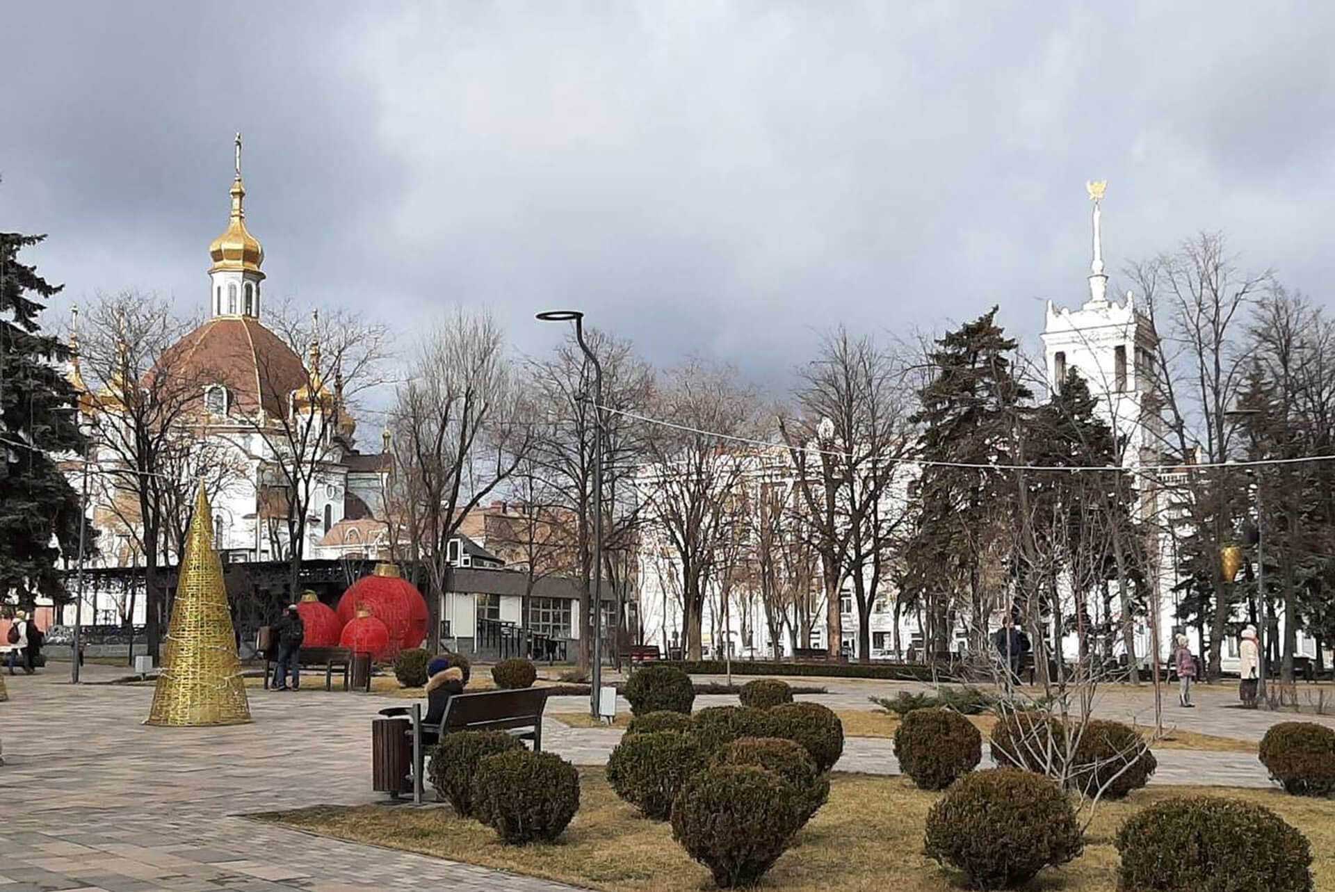 A church with a golden turret behind a landscaped plaza with topiary