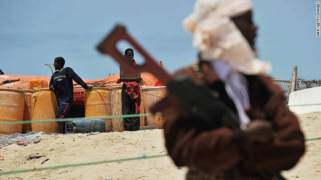 A pirate folds his arms over his weapon near two boys on a beach in the Somali town of Hobyo on August 20, 2010. 