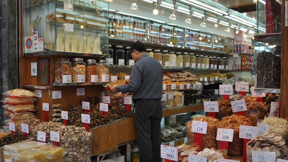 A shop owner works in his dried seafood store, where dried shark fins are displayed in a glass case. 