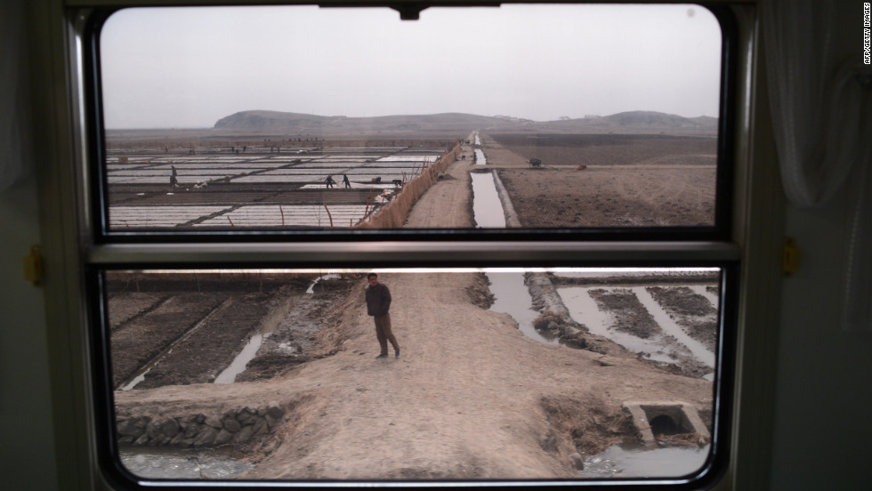 Workers and farms are seen through the window of a train as it passes through the country.