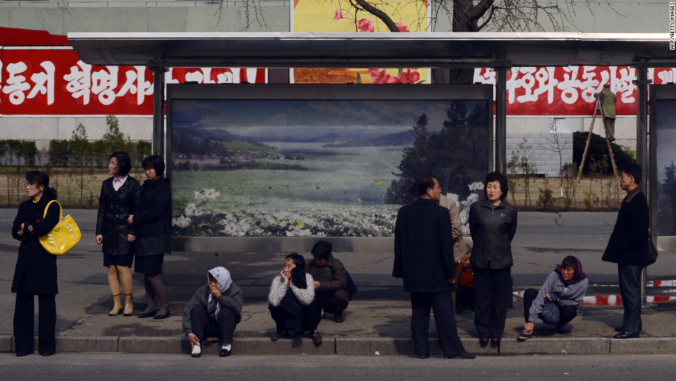 People line the street as they wait for a bus.