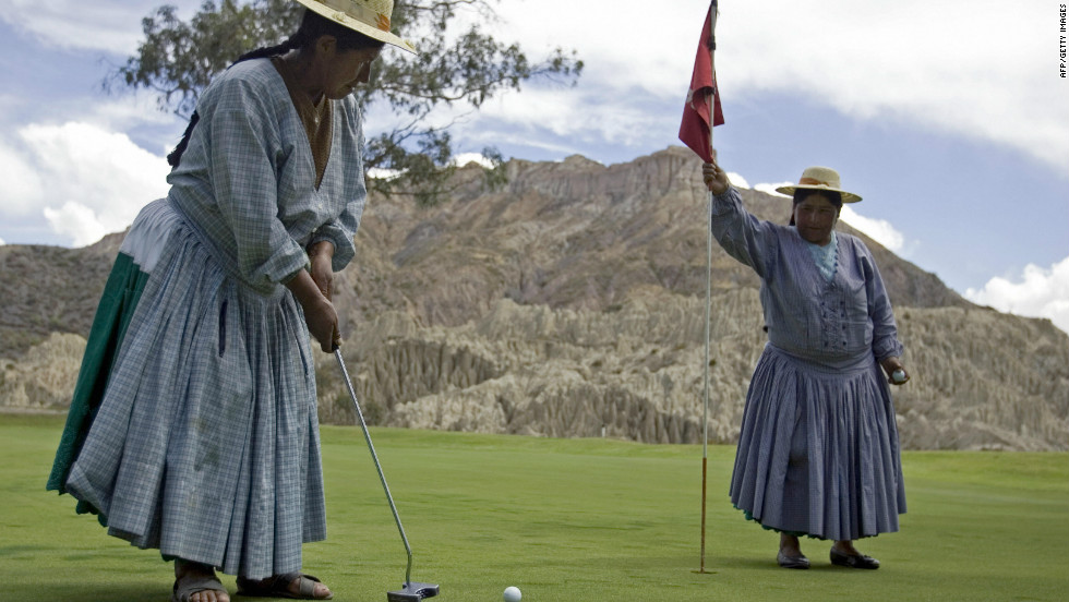 An  indigenous Aymara woman plays an approach shot as her colleague holds the flag.