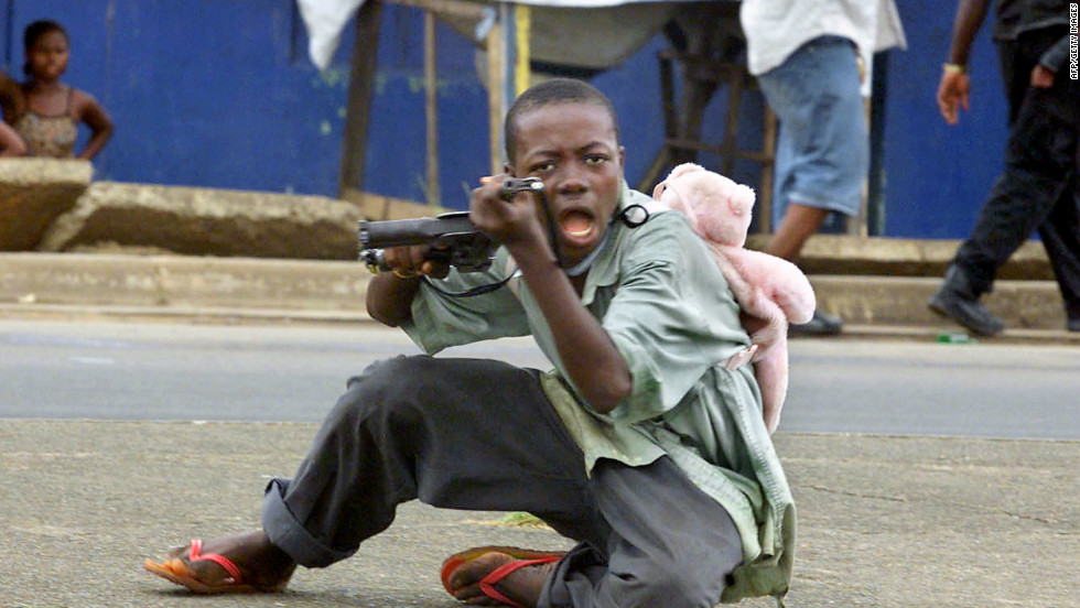 A child soldier wearing a teddy bear backpack points his gun at a photographer in a street of Monrovia in June 2003.