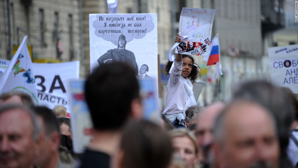 A young girl hoisted on someone&#39;s shoulders holds up a sign during the demonstration.