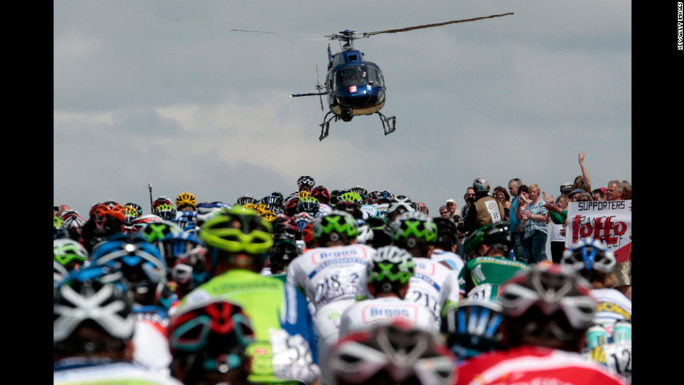 Fans cheer and a television helicopter flies above as the riders stream by.