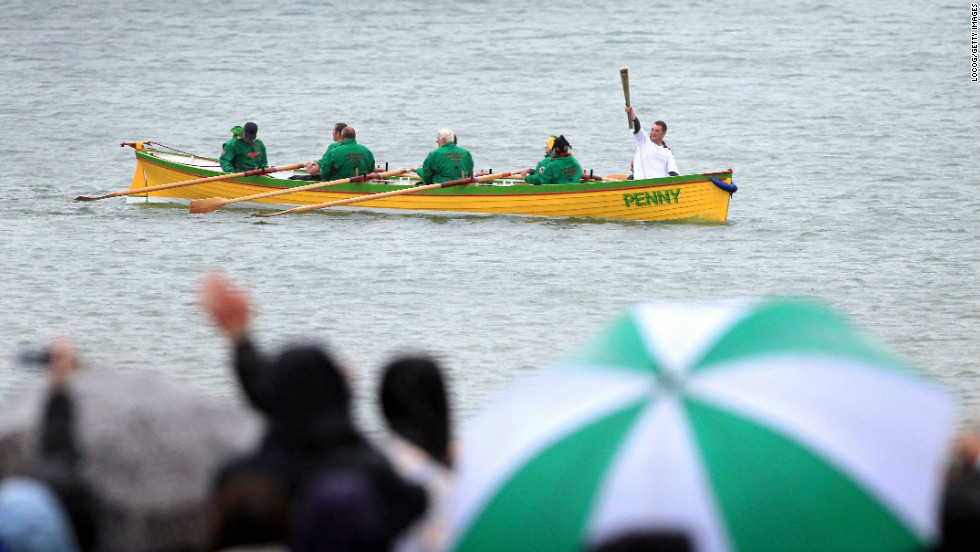Ryan Hope carries the torch Thursday, July 12, on the row boat Penny off the waters of Weymouth.