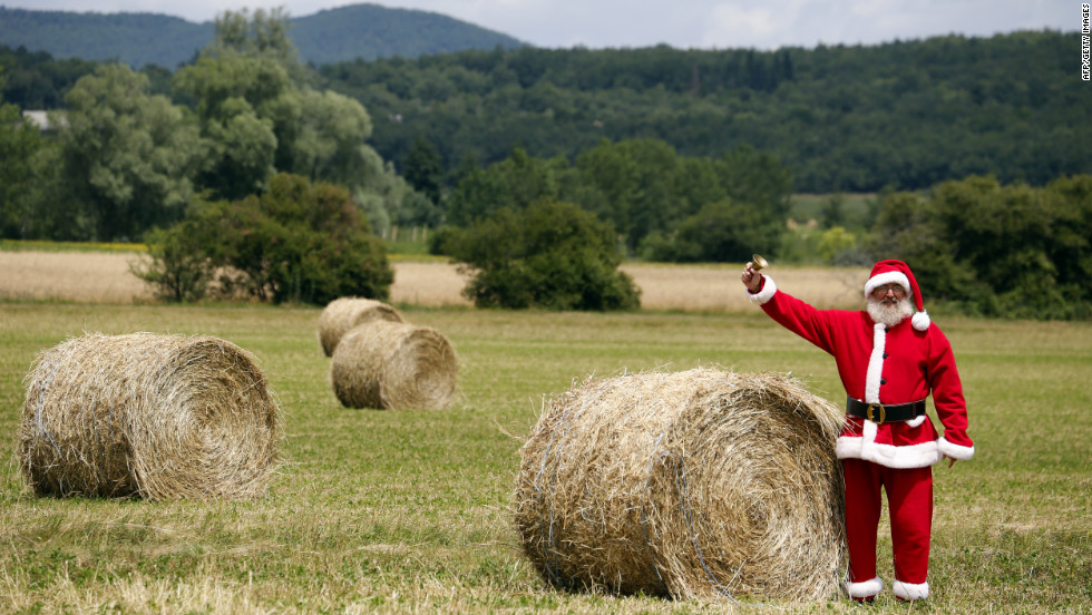 A spectator dressed as Santa Claus rings a bell from a field along the race route as riders pass by.