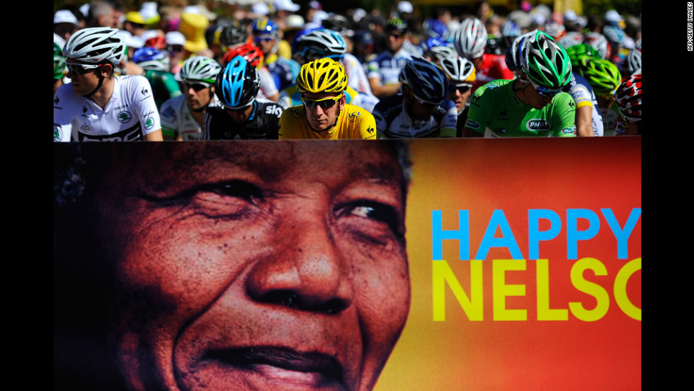 Race leader Bradley Wiggins of Great Britain, in yellow, and the main pack of riders pass a Nelson Mandela birthday banner Wednesday. People around the globe celebrated Mandela&#39;s 94th birthday.