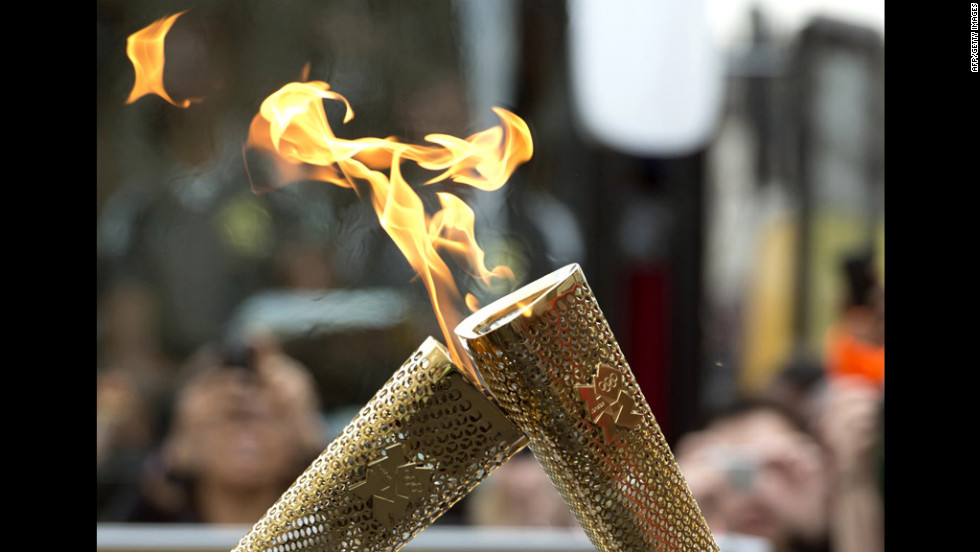 Torchbearers &quot;kiss&quot; their torches to pass the Olympic flame during the London 2012 torch relay through the Borough of Tower Hamlets in London on Saturday, July 21.