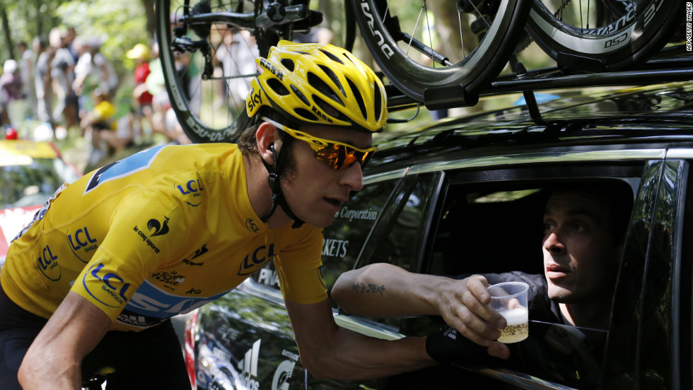 Overall race leader Bradley Wiggins of Great Britain rides next to a team car with a team member carrying a cup of Champagne during the final stage.