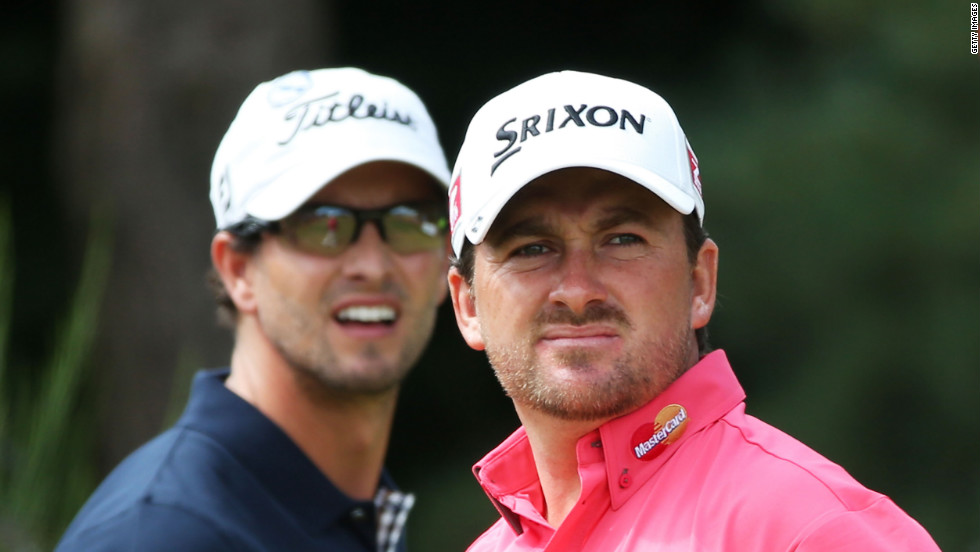 Graeme McDowell of Northern Ireland watches his tee shot on the second hole as Scott looks on.