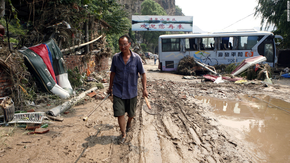 A man slogs through mud past damaged vehicles after flooding Tuesday, July 24, in Laishui, China, north of Beijing. The heaviest rain in 60 years submerged large parts of the Chinese capital. 