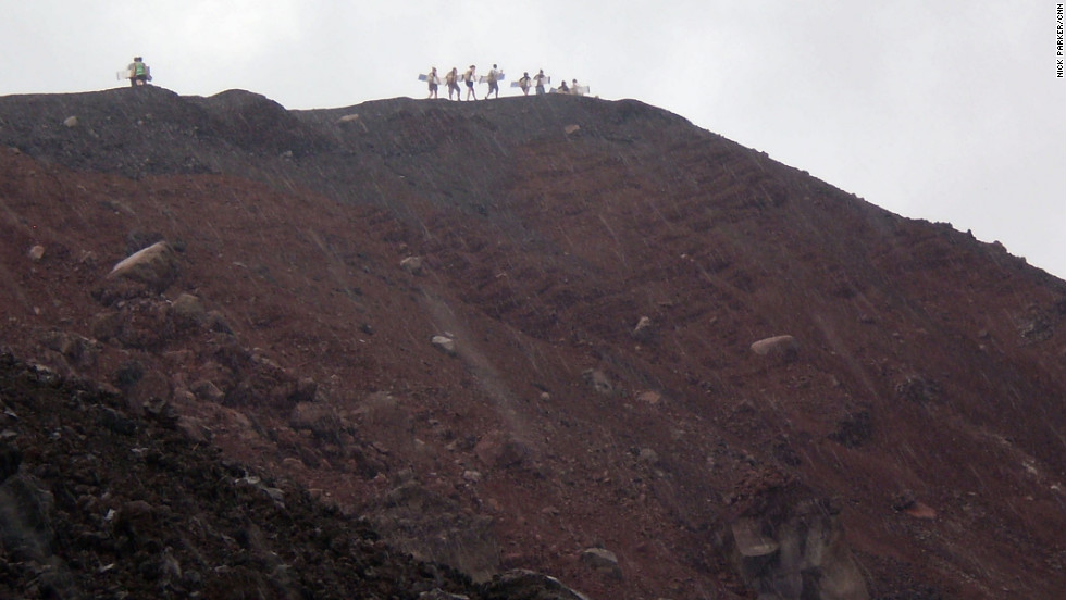 Surfers carry their wooden boards along the volcano&#39;s ridge.