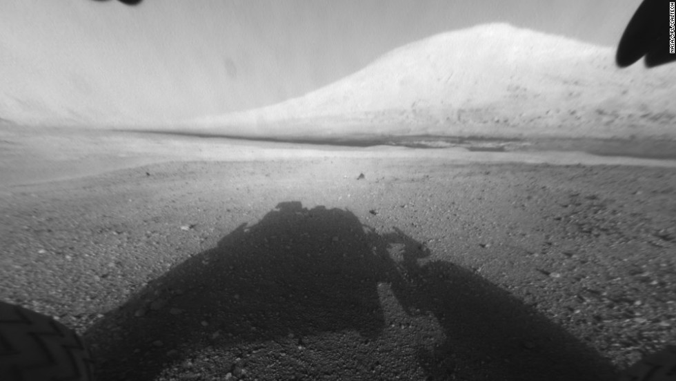 This image shows Curiosity&#39;s main science target, &quot;Mount Sharp.&quot; The rover&#39;s shadow can be seen in the foreground. The dark bands in the distances are dunes. 