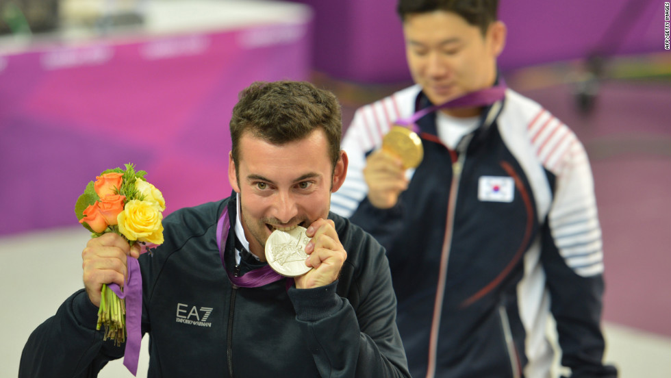 Italy&#39;s Luca Tesconi bites his silver medal as gold medalist South Korea&#39;s Jin Jong-oh stands behind him. They competed in the 10-meter air rifle men&#39;s final. 