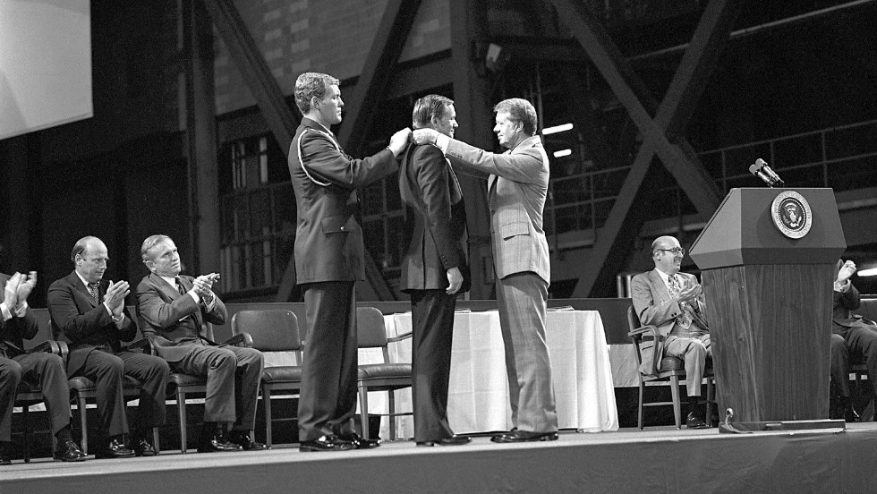 Armstrong receives the first Congressional Space Medal of Honor from President Jimmy Carter, right, assisted by Capt. Robert Peterson, on October 1, 1978. Armstrong, one of six astronauts to be presented the medal during ceremonies held in the Vehicle Assembly Building (VAB), was awarded for his performance during the Gemini 8 mission and the Apollo 11 mission.