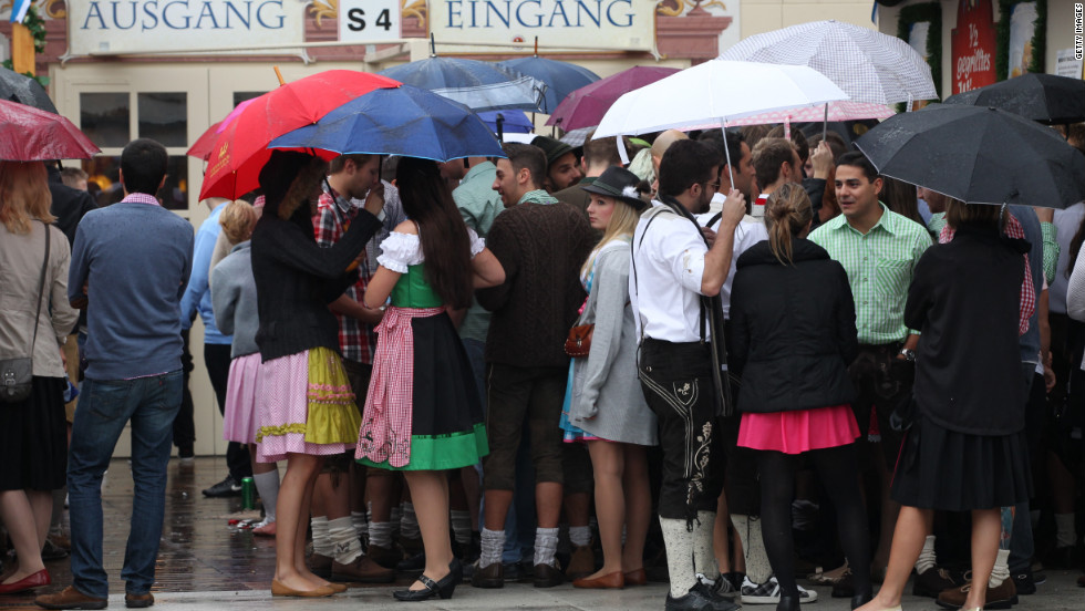 Visitors hold umbrellas as they wait in front of a beer tent.