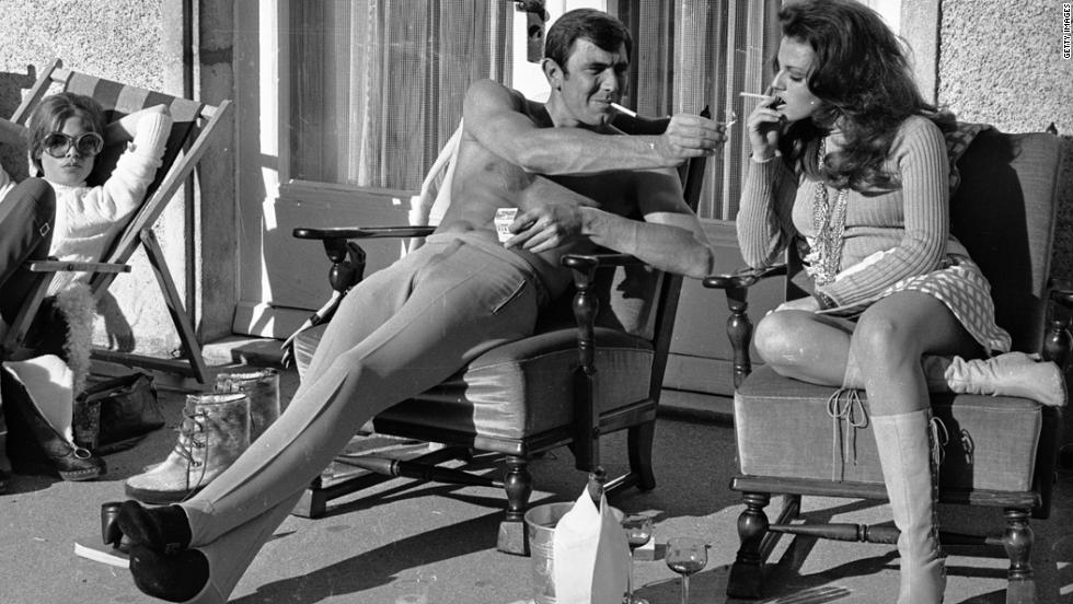 George Lazenby offers co-star Helena Ronee a light during the filming of &quot;&#39;On Her Majesty&#39;s Secret Service&quot; in the Swiss Alps in October 1968.