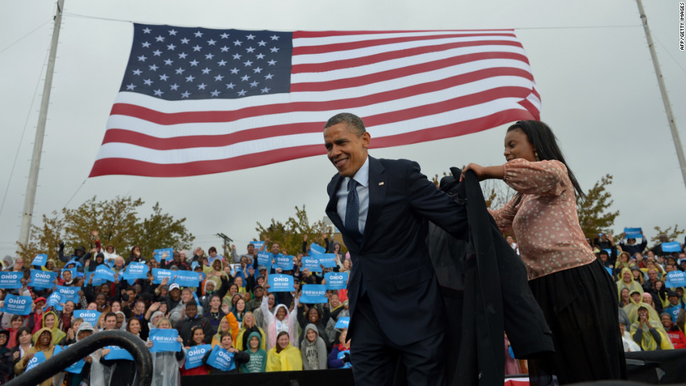 Obama is assisted with putting on a raincoat onstage during a campaign rally at Cleveland State University on Friday.