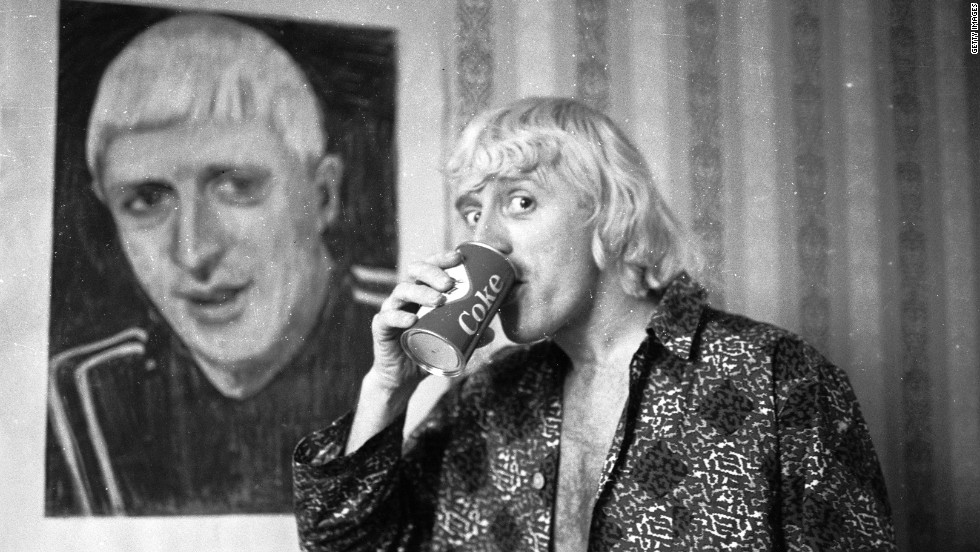 The first presenter of long-running music program &quot;Top of the Pops,&quot; Savile poses by a portrait of himself in February 1965, while enjoying his regular breakfast of Coke and a cigar in a central London hotel room.