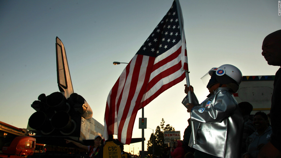 Amir Morris, 3, wears an astronaut costume while holding an American flag as the space shuttle crawls past.