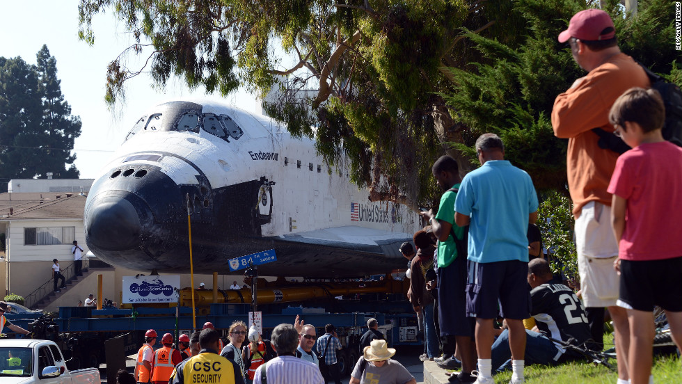 People watch as the shuttle makes its way up a narrow street.