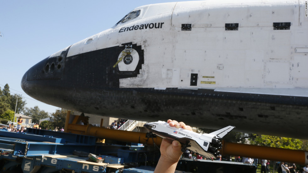 A boy holds a model of  Endeavour as the real thing rolls past.