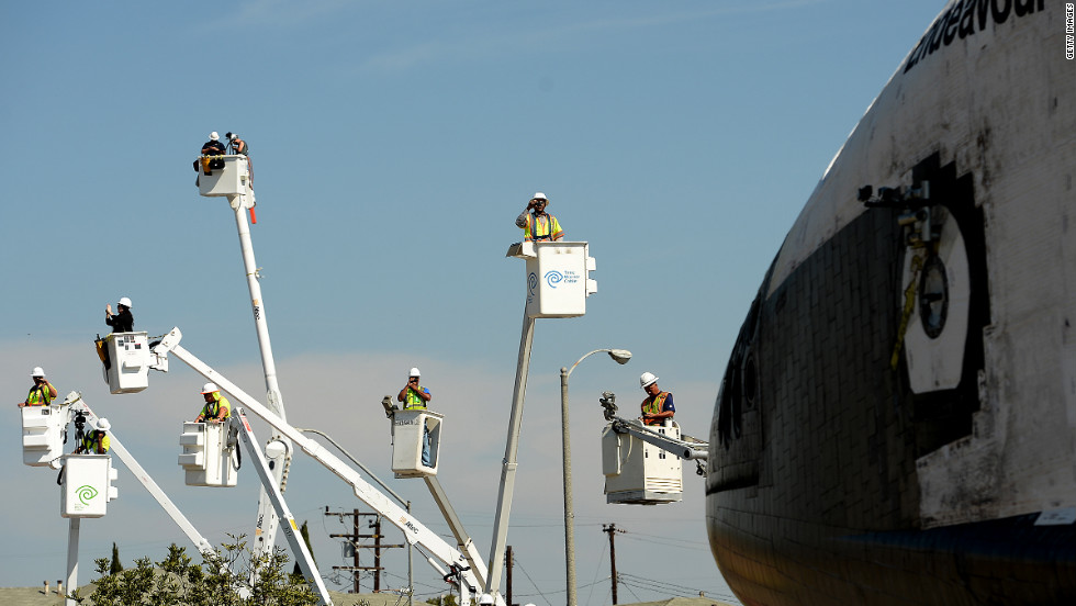 People take photos from cherry pickers Saturday as the shuttle moves along Crenshaw Drive in Inglewood, California.