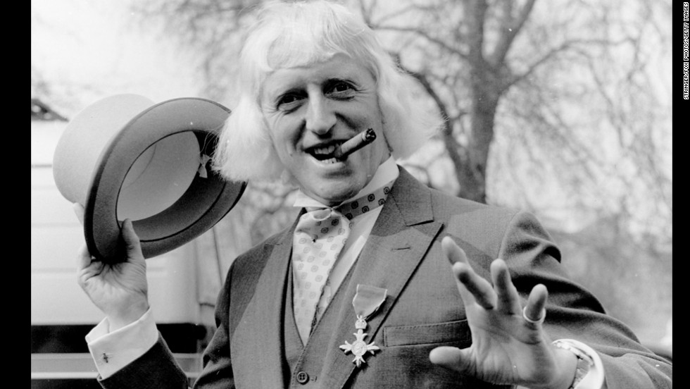 British radio disc jockey, television star and charity fund-raiser Sir Jimmy Savile poses for a photo at Buckingham Palace, London, after receiving the Order of the British Empire in 1972. Since his death a year ago at age 84, Savile has been knocked off his perch as a national treasure, accused of being a predatory pedophile who used his fame and position to abuse youngsters, sometimes on BBC premises.