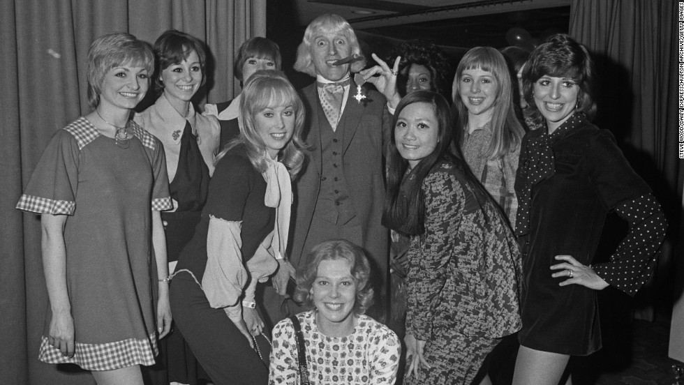 Savile shows off his Order of the British Empire to members of the &quot;Second Generation&quot; song and dance troupe.