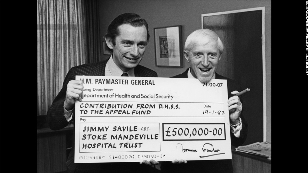 British Secretary of State for Social Services Norman Fowler presents Savile with a check for half a million pounds in 1982 as the government&#39;s contribution to an appeal for a new spinal injuries unit at Stoke Mandeville Hospital.