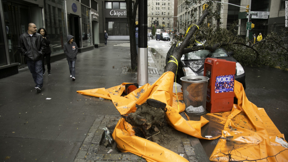 Passers-by look at a car that was crushed by a tree near New York&#39;s financial district on Tuesday.