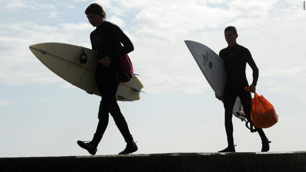 Dean Walter, left. and Henry Young walk along a seawall in Scituate, Massachusetts, with their surfboards after going into the heavy surf for about 20 minutes on Tuesday.