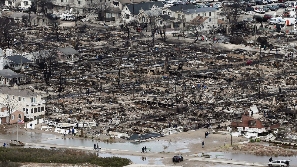 People walk near the remains of burned homes in the Breezy Point neighborhood of Queens, New York, on Wednesday.