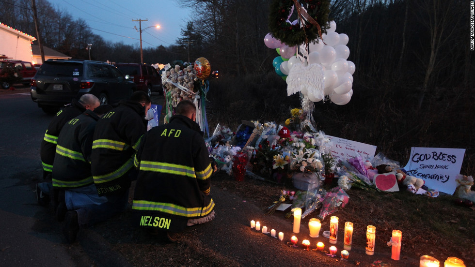 Firefighters kneel to pay their respects at a makeshift memorial near the school in Newtown on Saturday.