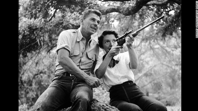 1954:  EXCLUSIVE American actor Ronald Reagan watches as his wife, Nancy, aims a rifle while they sit on a large rock outdoors at their ranch in Malibu, California. Both wear jeans and their shirt sleeves rolled up.  (Photo by Murray Garrett/Getty Images)