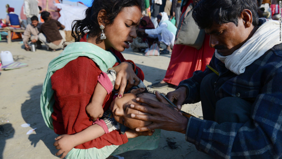 An Indian devotee holds her child as a man shaves his head on February 9.