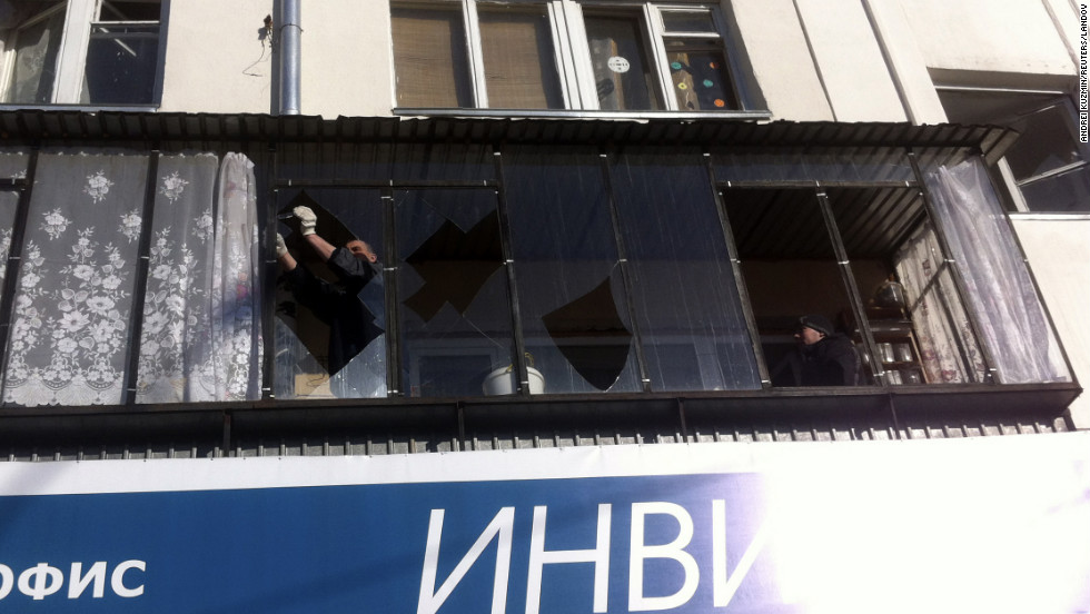 A man removes shards of glass from the frame of a broken window. 