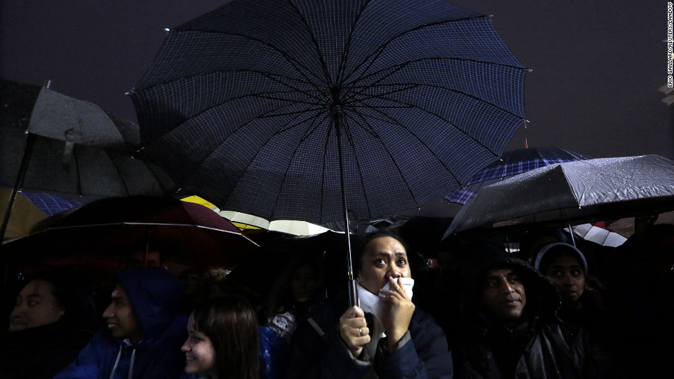 People under umbrellas react to the news while waiting for the new pope to appear.