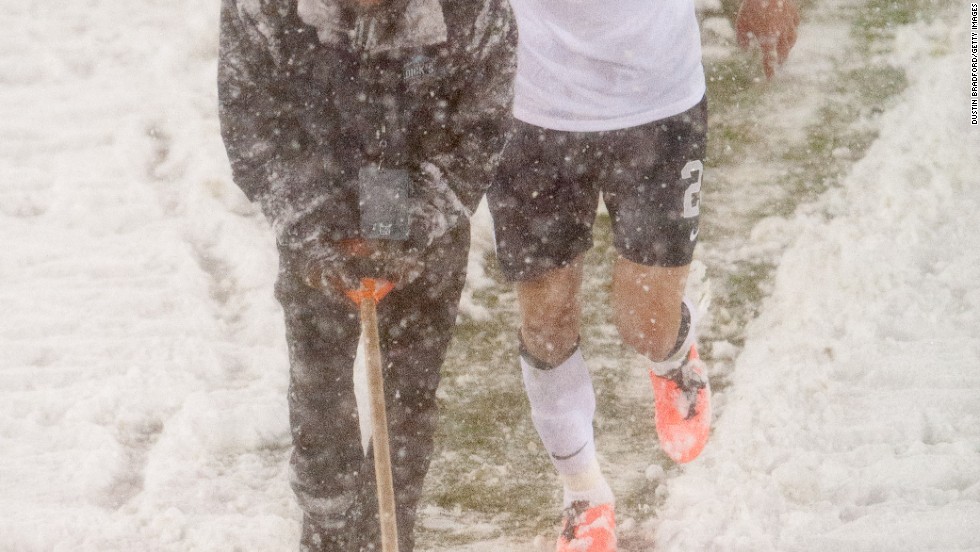 U.S. midfielder Geoff Cameron lends a hand as an official attempts to clear snow off the pitch markings.