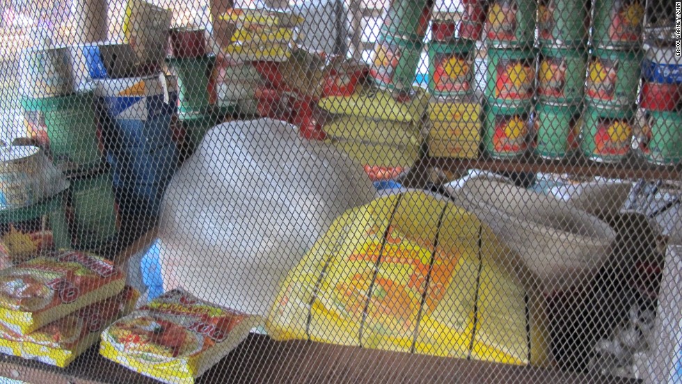 Through a wired screen sit convenience items in this Makoko-style corner store. Instant noodles, rice, canned goods, fruits and vegetables are all on sale in a structure that also houses a family.
