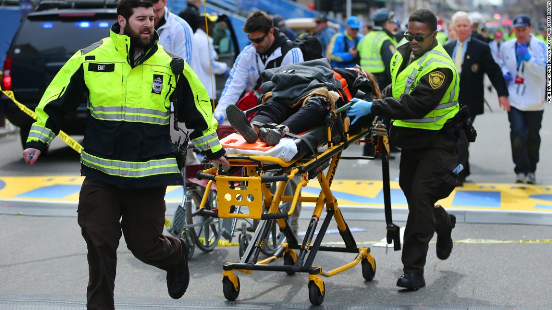 A bystander who was injured in the first explosion is wheeled across the finish line while receiving medical attention from rescue workers.
