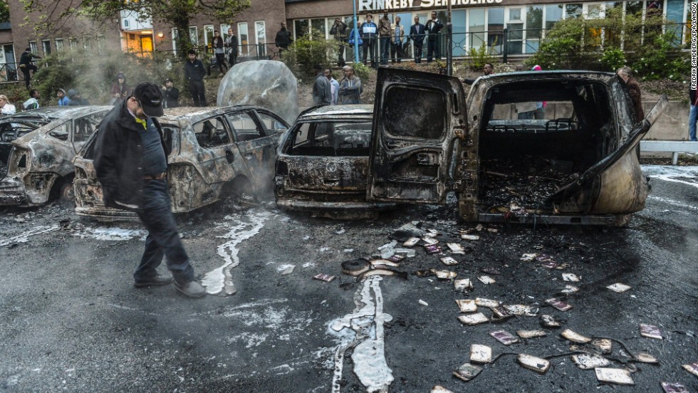 A man examines the debris around a row of burnt cars in the Stockholm suburb of Rinkeby on Thursday, May 23.