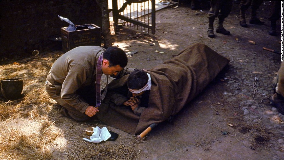 A U.S. Army chaplain kneels next to a wounded soldier to administer the eucharist and last rites, France, 1944.