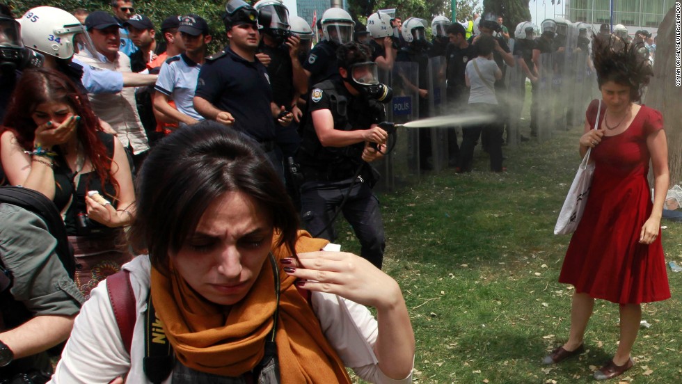 A riot police officer uses tear gas as people protest the destruction of a park for a pedestrian project in Istanbul&#39;s Taksim Square on May 28, 2013. The woman in red became the face of the protests.