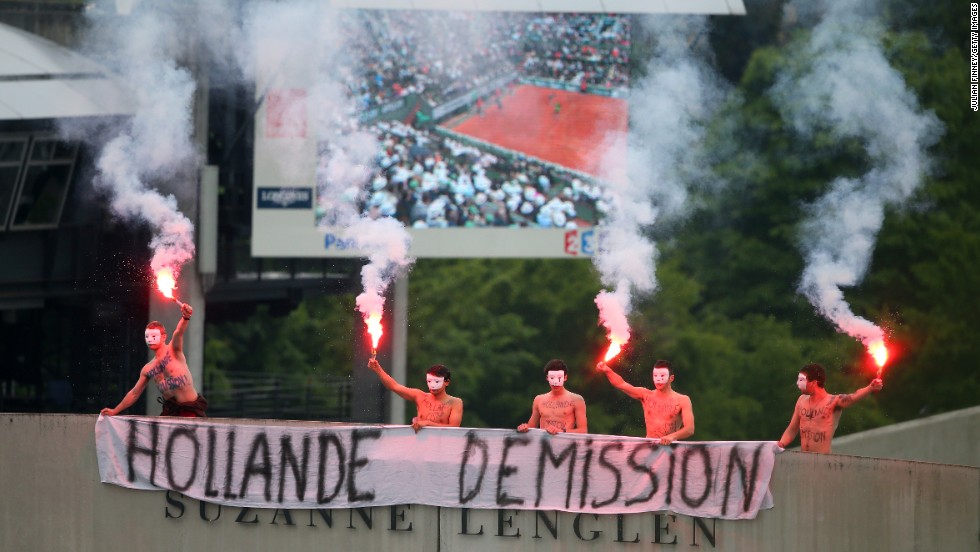 Protesters light flares and unfurl a banner which calls for the French President Francois Hollande&#39;s resignation on the top of Court Suzanne Lenglen as Nadal and Ferrer compete.