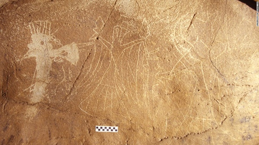 An upright bird figure has arms and hands and holds ceremonial weapons aloft, flanked by axes with blades coming out of human faces, in this Tennessee cave painting from the 14th century. 