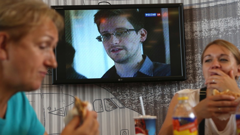 Transit passengers at Sheremetyevo airport in Moscow eat at a cafe: Edward Snowden is seen on a TV screen in the background. 